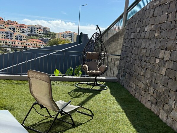 A balcony with artificial grass, a hanging chair, and a cushioned chair.