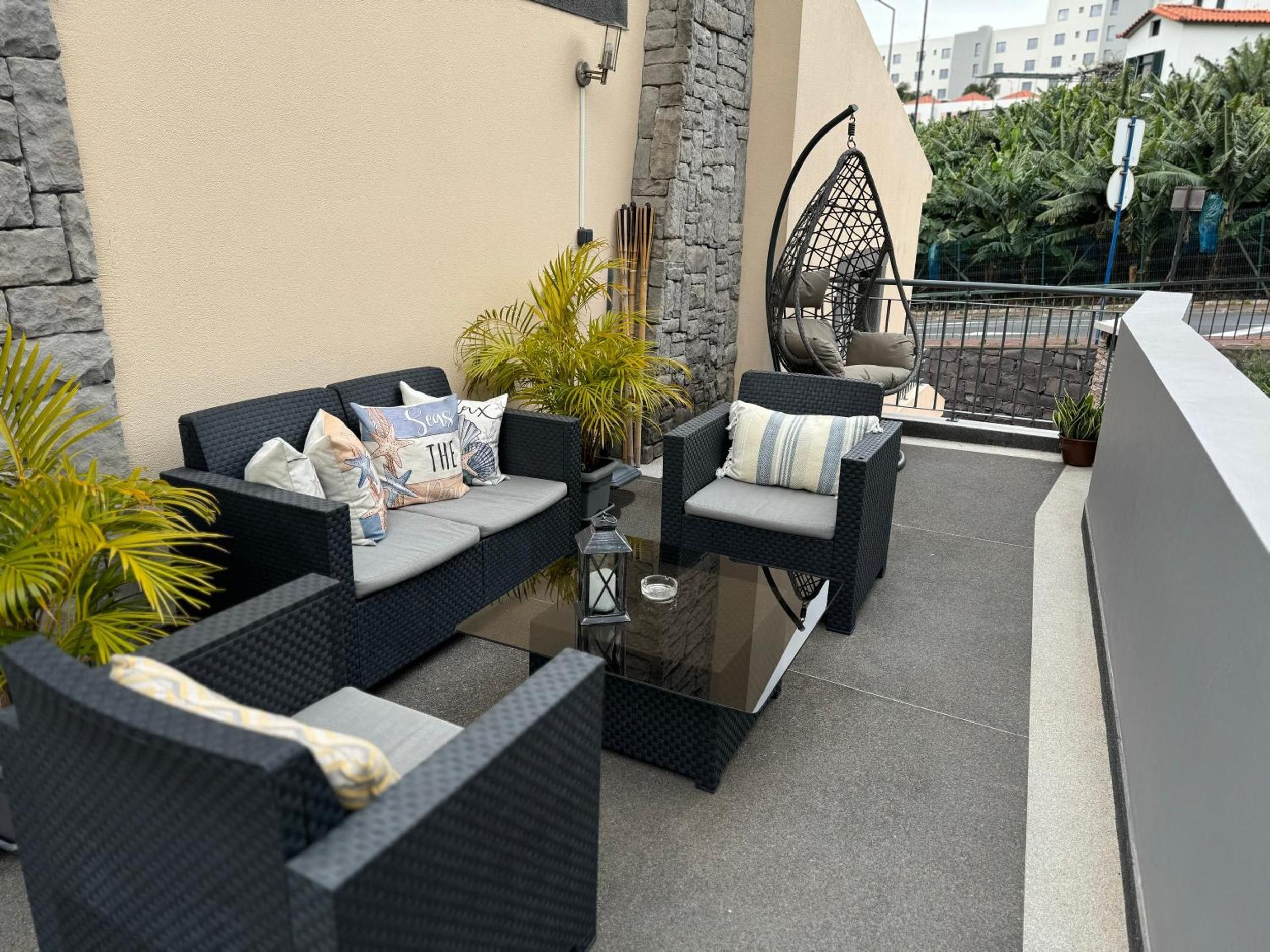 Un espacio al aire libre con mobiliario de mimbre, cojines y una mesa de vidrio.