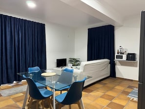 Un espacio habitable compacto con comedor, sofá, televisor y kitchenette.