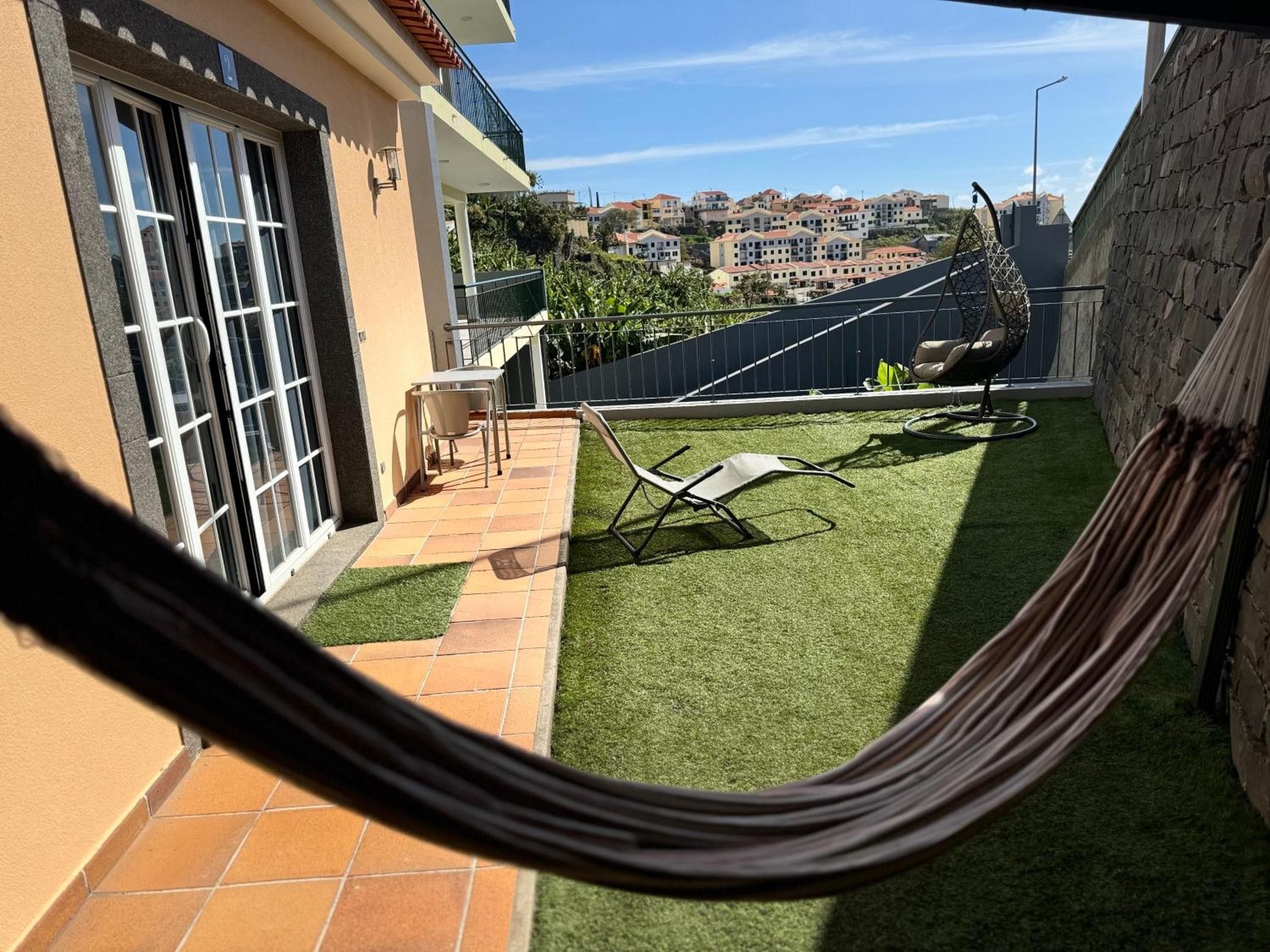 Zona residencial con un pequeño patio trasero con césped artificial, una hamaca y una terraza con mesa y sillas.