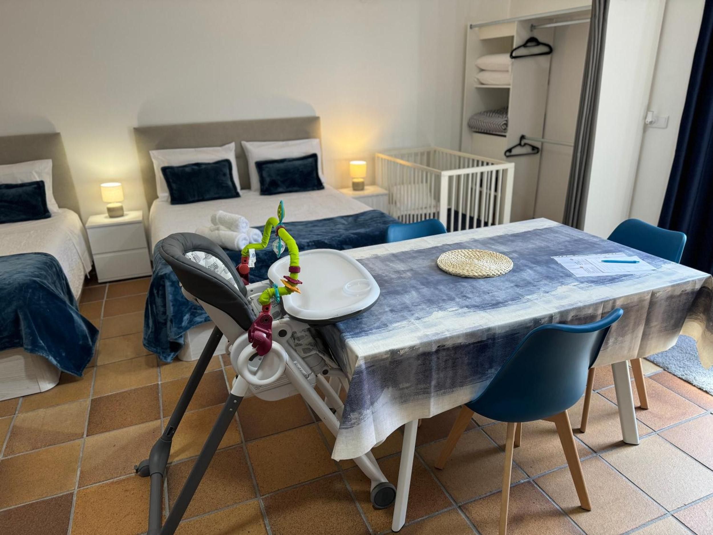 Una habitación de hotel con una mesa de comedor, sillas, una cuna y una cama con almohadas.
