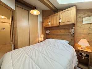 A bedroom with a bed, wooden headboard, bedside lamps, and a wardrobe. - 3rd floor, balcony, tv, ski locker, 28m², Praz sur Arly (Praz-sur-Arly)