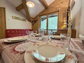 A dining table set for four with plates, glasses, and cutlery, in a room with wooden beams and a window. - 3rd floor, balcony, tv, ski locker, 28m², Praz sur Arly (Praz-sur-Arly)