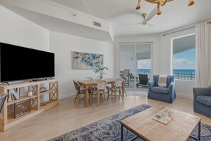 Ein modernes Wohnzimmer mit Flachbildfernseher, Esstisch, Stühlen, Couchtisch und Blick auf den Ozean.