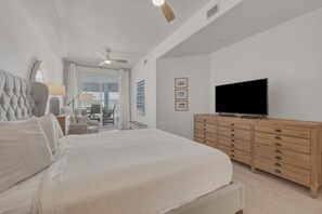 Ein Schlafzimmer mit einem großen Bett, einer Holzkommode, einem Flachbildfernseher und einem Balkon mit Sitzmöbeln.