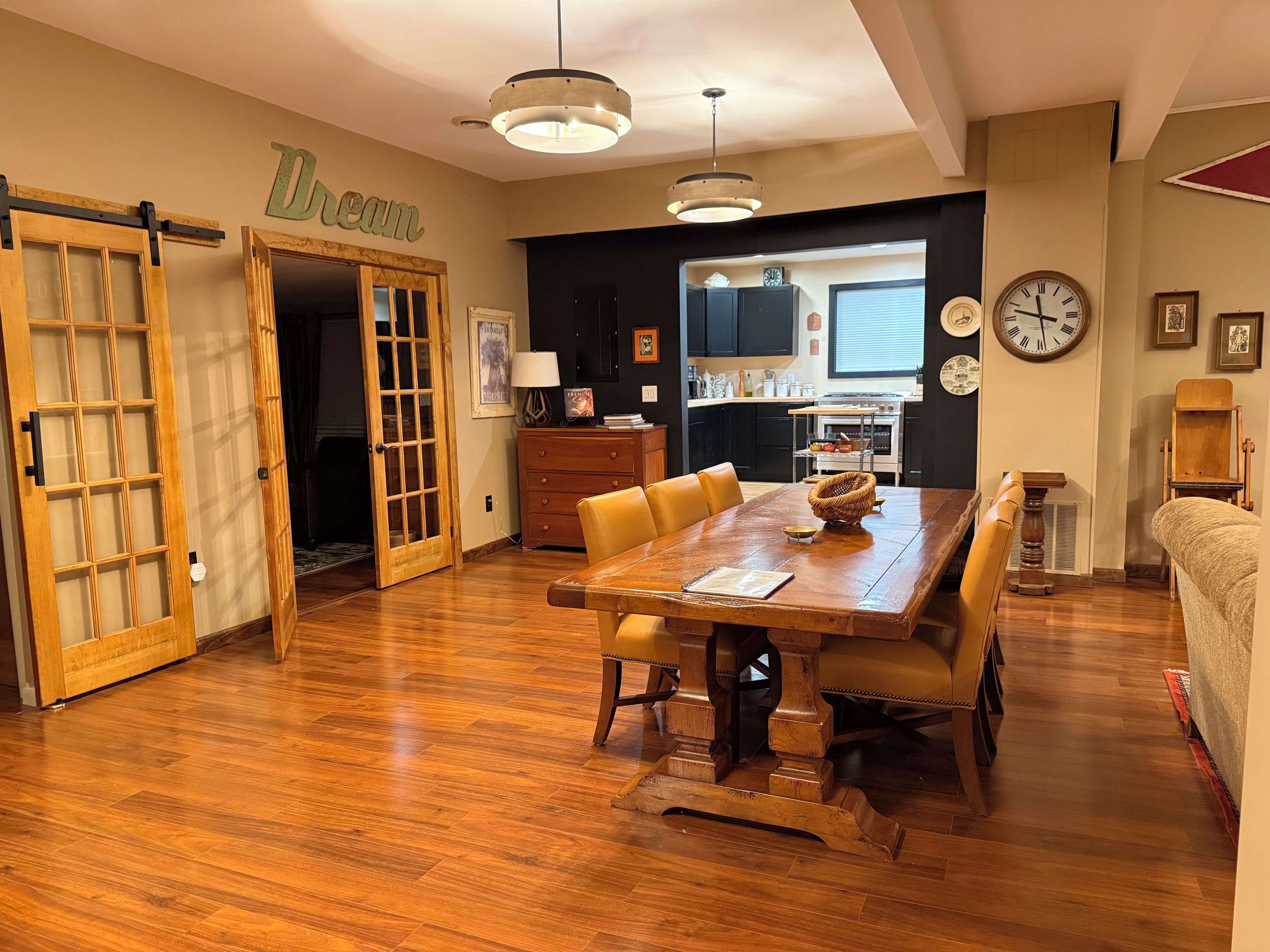 Un comedor con una mesa y sillas de madera, una cocina al fondo y una puerta con la etiqueta 'Dream'.