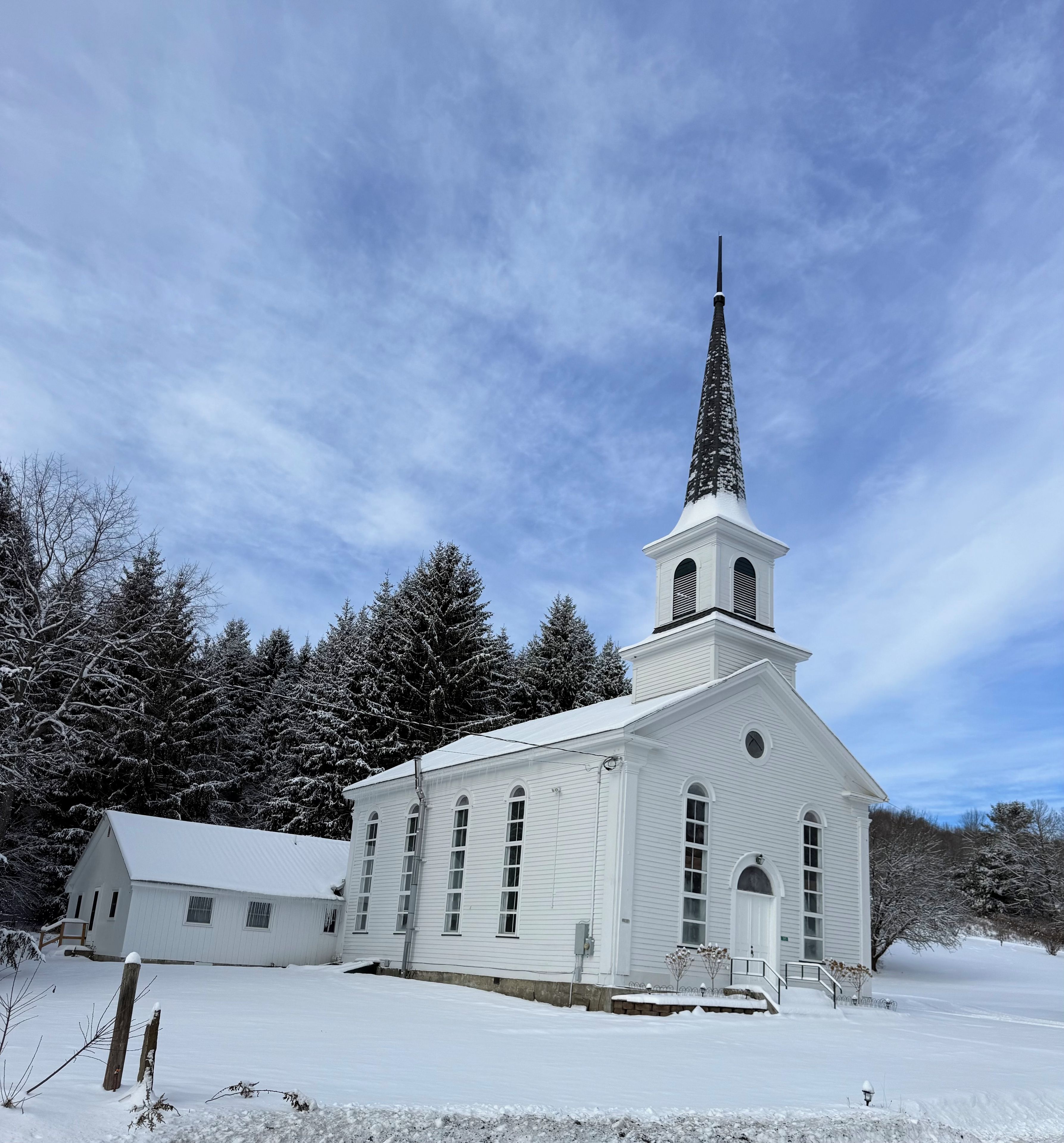 Une église blanche, dotée d’un clocher et d’un campanile, entourée d’arbres couverts de neige.