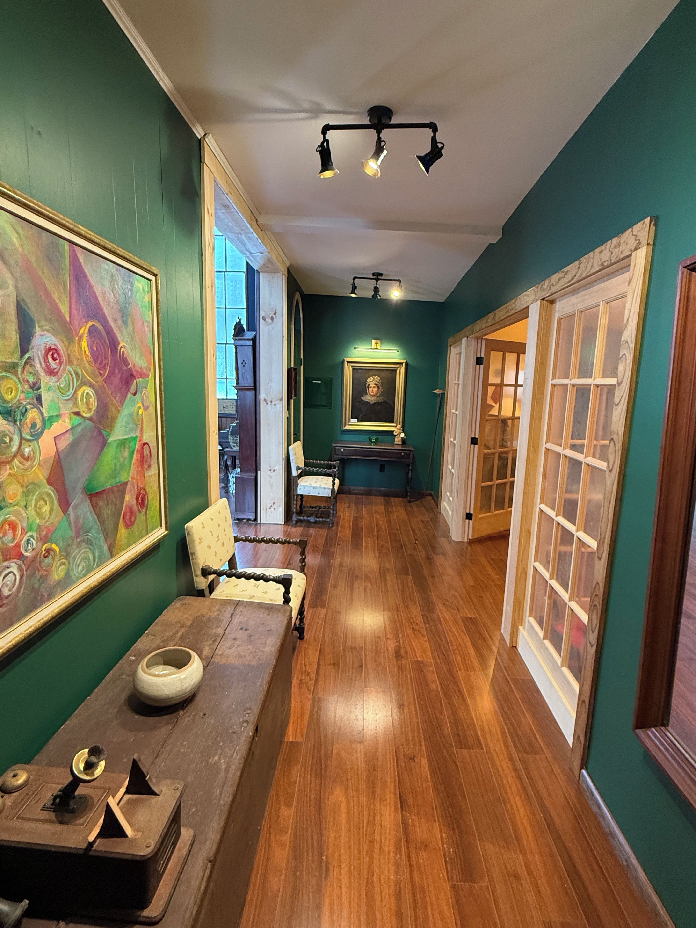 A hallway with wooden flooring, a table with a bowl and a model, a chair, and a painting on the wall.