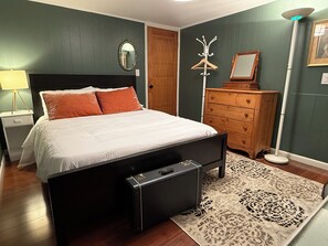 Un dormitorio con cama, cómoda, espejo, perchero y lámpara.