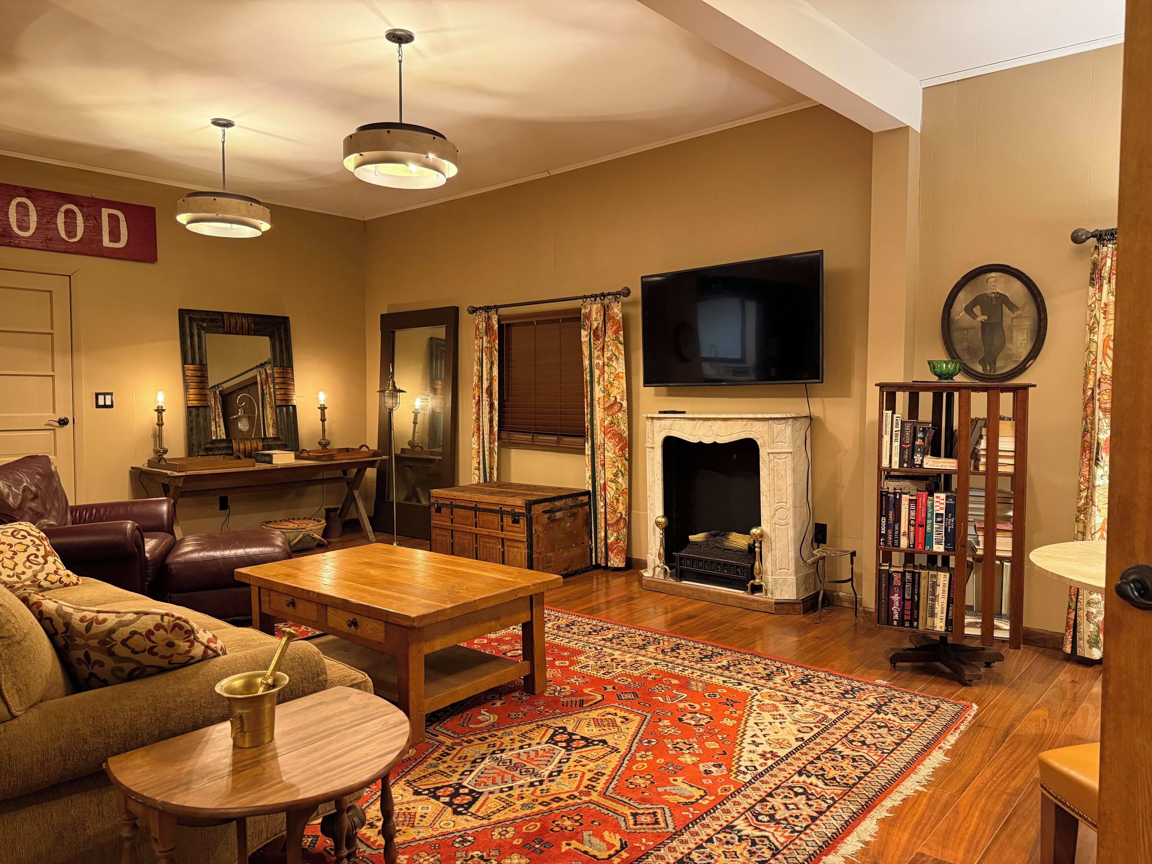 A cozy living room with a fireplace, a television, a bookshelf, and a patterned rug.