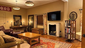 A cozy living room with a fireplace, a television, a bookshelf, and a patterned rug.