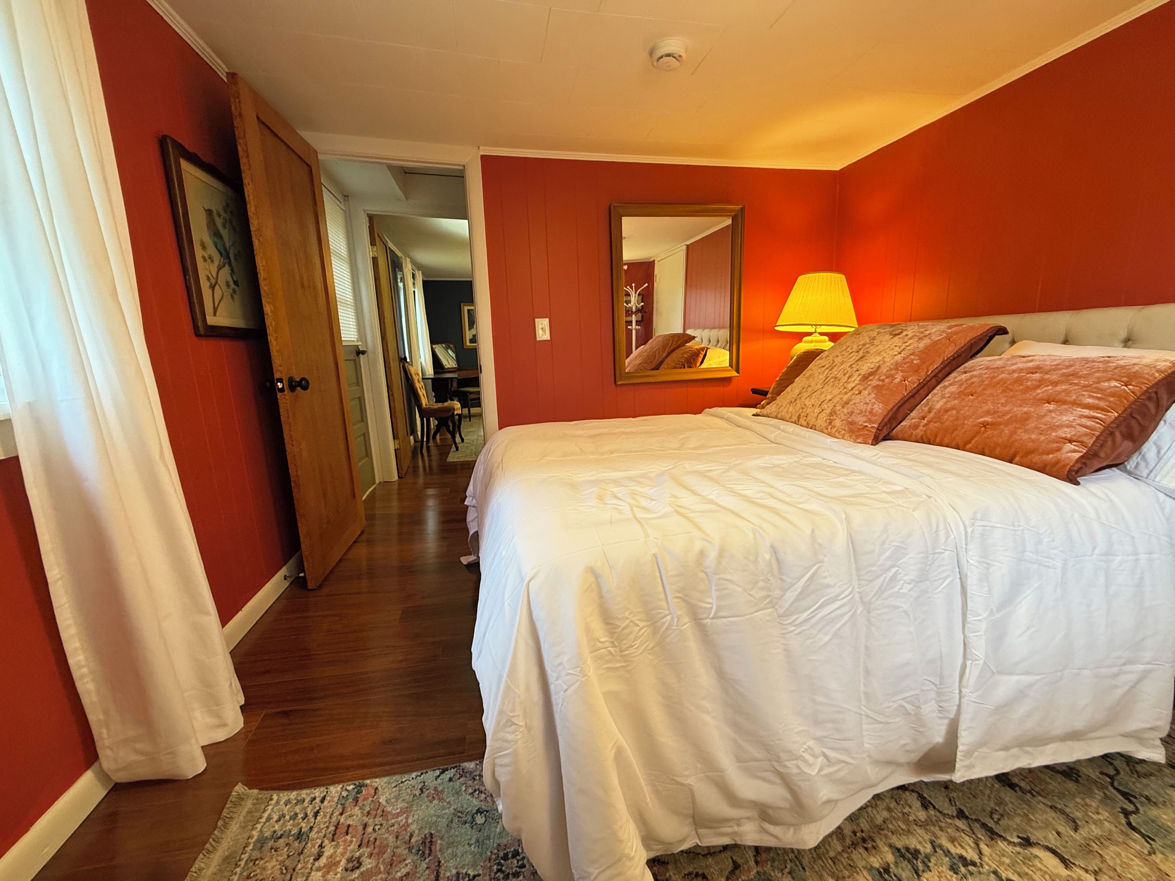 A hotel room with a bed, a nightstand, a lamp, a mirror, and a door leading to another room.