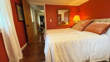 A hotel room with a bed, a nightstand, a lamp, a mirror, and a door leading to another room.