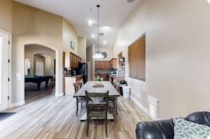 A spacious living area with a pool table, a dining table with chairs, and a kitchen in the background. - Desert Retreat | Pool, Near Spring Training (Surprise)