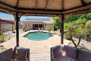 A covered outdoor area with a pool, lounge chairs, and a patio. - Desert Retreat | Pool, Near Spring Training (Surprise)