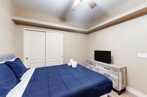 Ein Schlafzimmer mit einem Bett, einem Schminktisch, einem Fernseher und einem Deckenventilator.