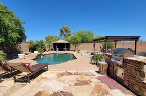 Ein Garten mit Swimmingpool, Grillplatz und Laube.
