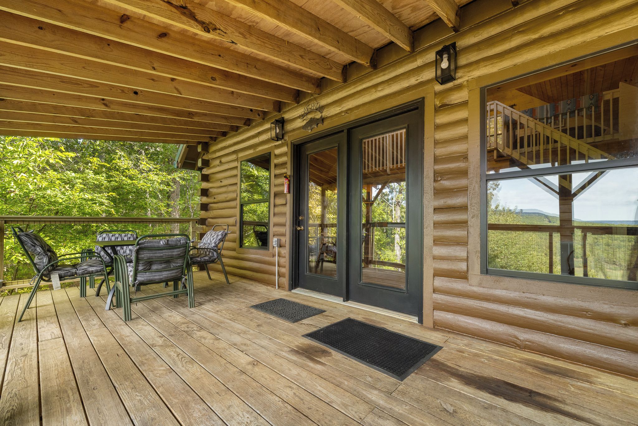 Une cabane en bois dotée d’un porche couvert, d’un escalier et offrant une vue sur la forêt environnante.