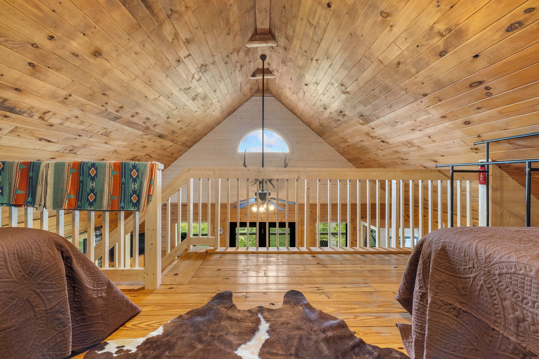 A spacious loft bedroom with a high ceiling, wooden beams, a skylight, a fireplace, and a view of the outdoors.