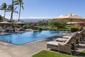 A pool area with lounge chairs and umbrellas, surrounded by palm trees and a view of the ocean. - Waikoloa, Kolea, Spacious 6 BR, Sleeps 16 (Waikoloa Village)