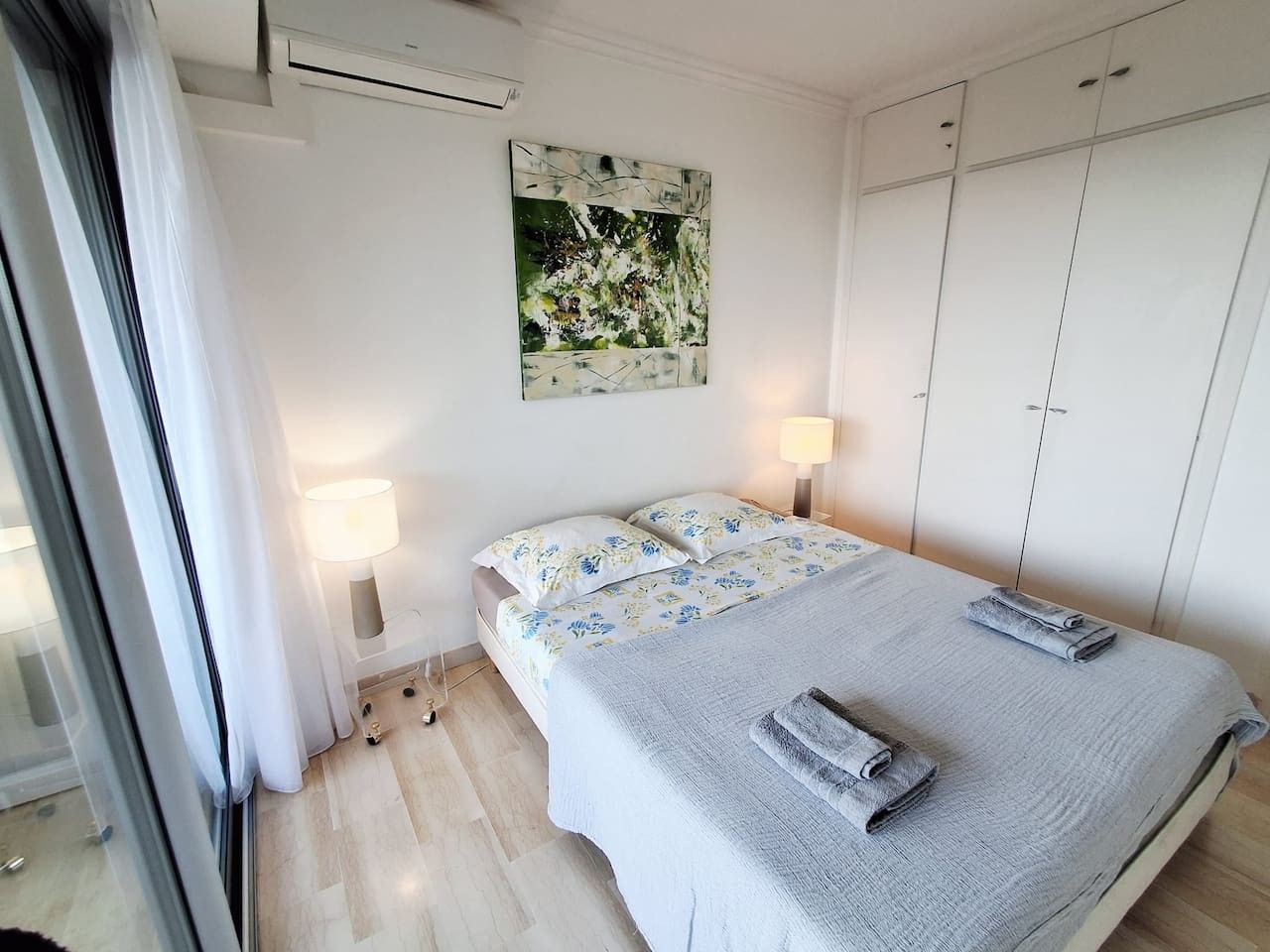 Une chambre à coucher comprenant un lit, deux lampes de chevet, un tableau décoratif et une armoire.