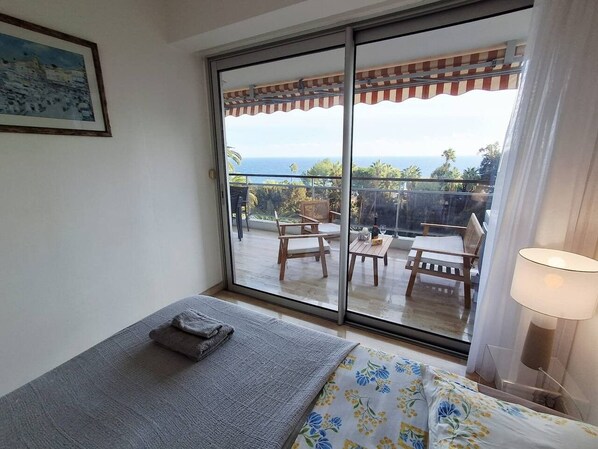 Una habitación con cama, ventana y vista a un patio exterior con mobiliario.