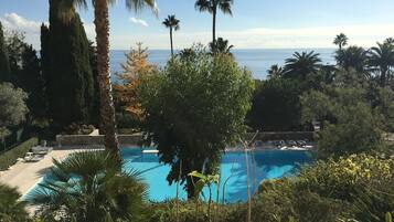 Une piscine entourée de palmiers et de cyprès, avec vue sur l’océan.