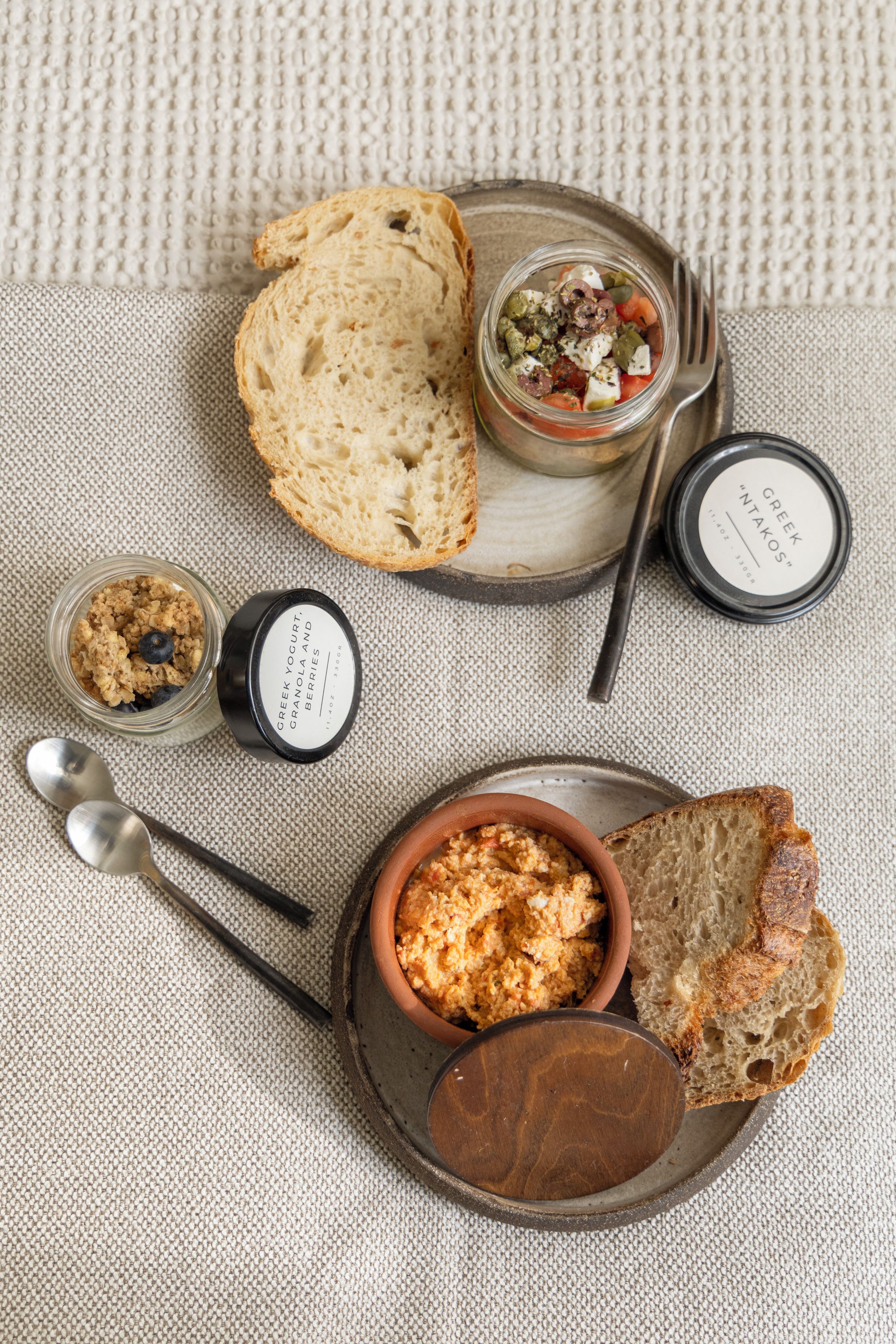 Un'impostazione con pane, un vasetto di yogurt greco, una ciotola di hummus e un piccolo contenitore di olive su un tappetino di vimini.