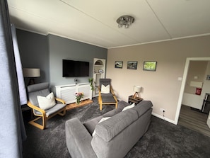 Un salon avec un canapé gris, une chaise en bois, un téléviseur et une petite table avec une lampe.