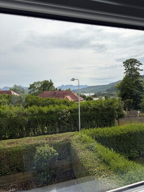 Blick aus einem Fenster auf eine Straßenlaterne, Grünflächen und entfernte Berge.