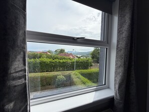 A window with a view of a green landscape, buildings, and mountains in the distance. - Kenmore is a lovely 3-bedroom house in Portree perfect for your getaway (Portree)