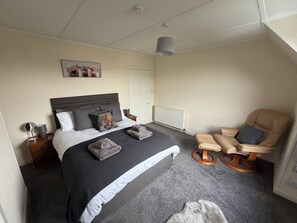 Ein Schlafzimmer mit einem Bett, Nachttischen, einem Sessel, einem Heizkörper und einer Deckenleuchte.