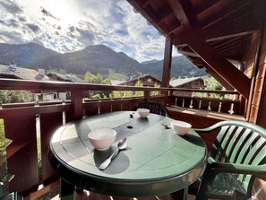 A round table with chairs and bowls on a balcony overlooking a mountainous landscape. - 2nd floor, swimming pool, balcony, tv, ski locker, 40m², Praz sur Arly (Praz-sur-Arly)
