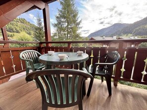 A wooden deck with a round table and chairs, overlooking a mountainous landscape. - 2nd floor, swimming pool, balcony, tv, ski locker, 40m², Praz sur Arly (Praz-sur-Arly)