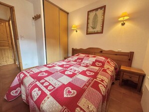 A bedroom with a bed, two bedside lamps, a wooden headboard, a nightstand, and a framed picture on the wall. - 2nd floor, swimming pool, balcony, tv, ski locker, 40m², Praz sur Arly (Praz-sur-Arly)