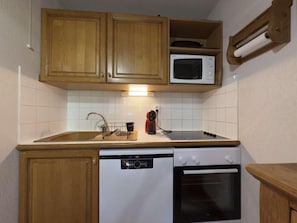 A compact kitchen with wooden cabinets, a microwave, a dishwasher, and an oven. - Ground floor, balcony, tv, ski locker, 35m², Praz sur Arly (Praz-sur-Arly)