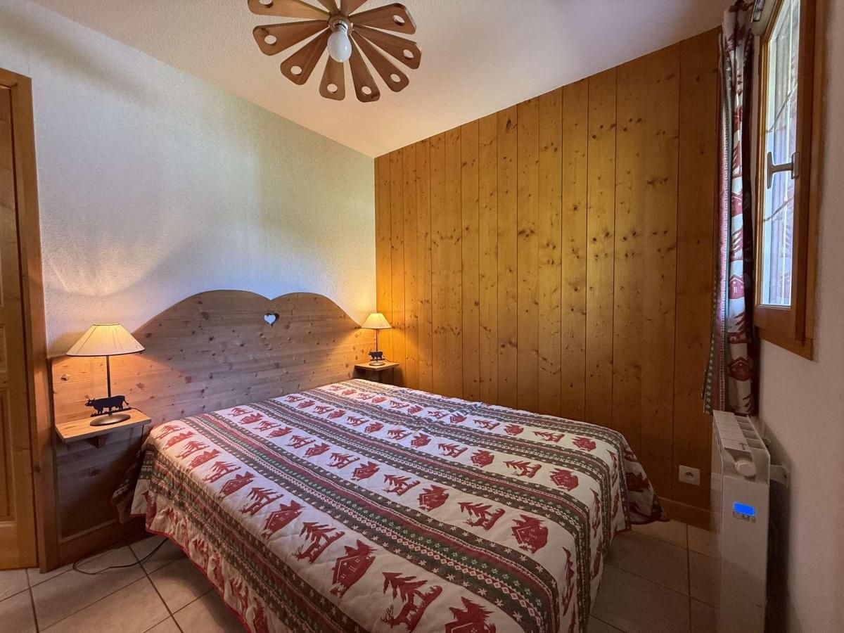 A bedroom with a wooden headboard, a bed with a patterned bedspread, two bedside lamps, and a ceiling fan.