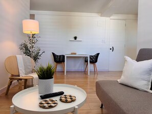 A modern living room with a sofa, a round coffee table with a plant and remote control, a dining area with a table and chairs, and a lamp. - Centrally located in historic town of San Germán! (San Germán)