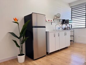 A modern kitchen with a stainless steel refrigerator, white cabinets, a potted plant, and a window with blinds. - Centrally located in historic town of San Germán! (San Germán)