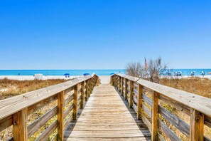 A wooden boardwalk leading to a beach with umbrellas and a flag. - Beachfront corner condo w direct gulf access, amazing views and ideal location (Gulf Shores)