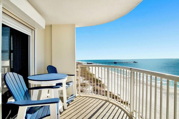 Un balcone con vista sulla spiaggia e un molo, con un tavolo e due sedie.