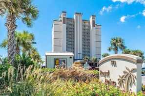 A high-rise hotel with multiple balconies, surrounded by tropical vegetation and a clear sky. - Beachfront corner condo w direct gulf access, amazing views and ideal location (Gulf Shores)