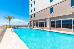 Una piscina adiacente a un edificio con numerose finestre e una palma.