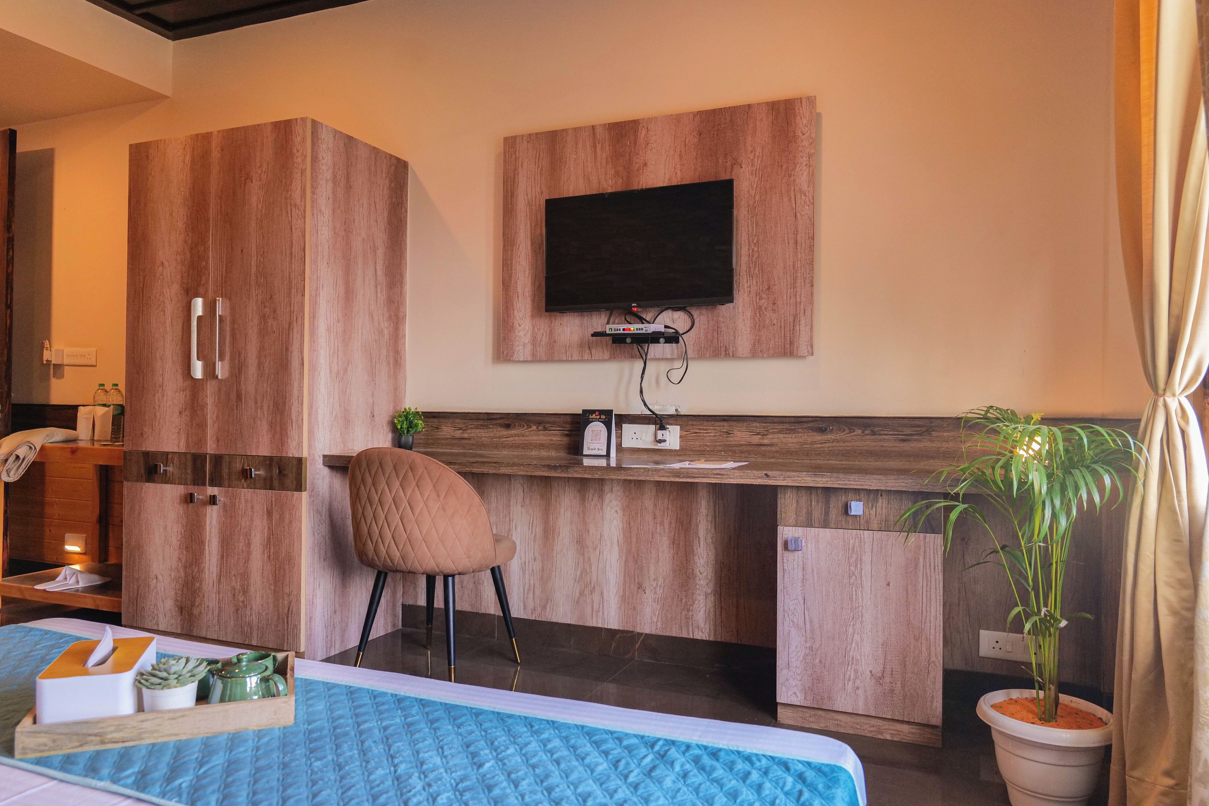 A hotel room with a bed, a desk with a chair, a television, and a potted plant.