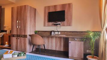 A hotel room with a bed, a desk with a chair, a television, and a potted plant.