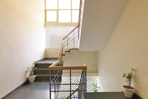 Een trap met een metalen leuning en een houten balustrade, die naar een bovenverdieping leidt. Er staan potplanten op de overloop en bij de trap.
