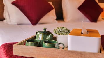 Bandeja con tetera, dos tazas, caja de pañuelos y una planta suculenta sobre una cama con almohadas rojas.
