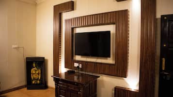 A room with a television mounted on a wooden panel wall, a small statue on a stand, and a door with a handle.