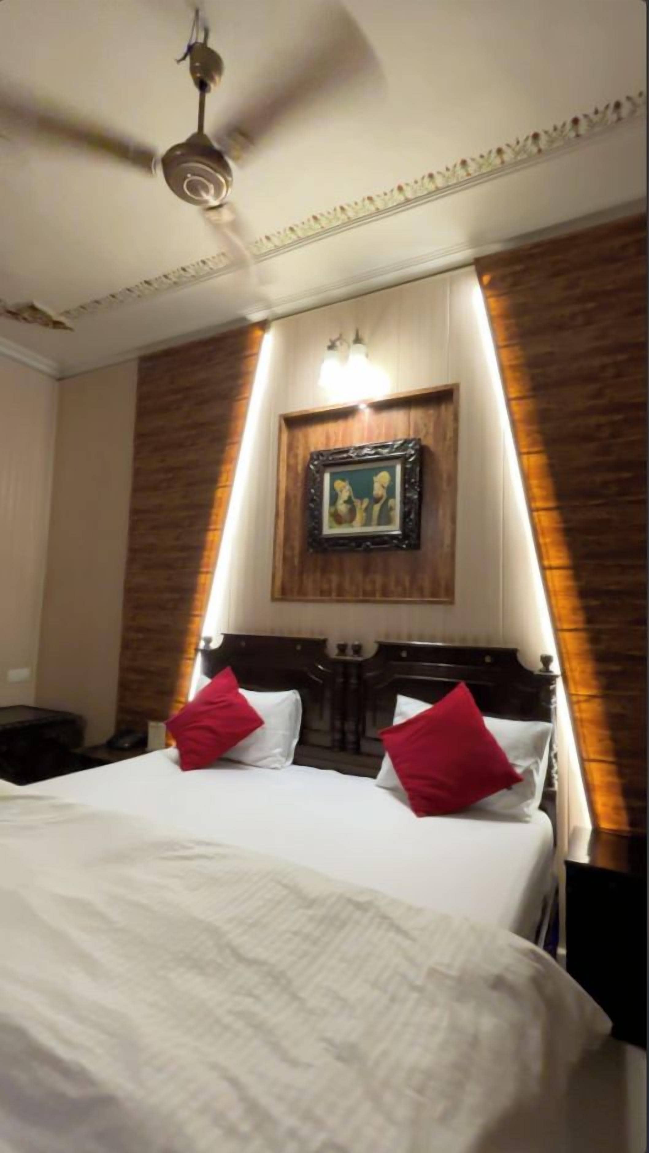 Une chambre d’hôtel avec un lit, un ventilateur de plafond, un tableau encadré au mur et un mur décoratif en bois.