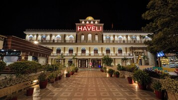Un hotel con entrada central, varios balcones y plantas en macetas.